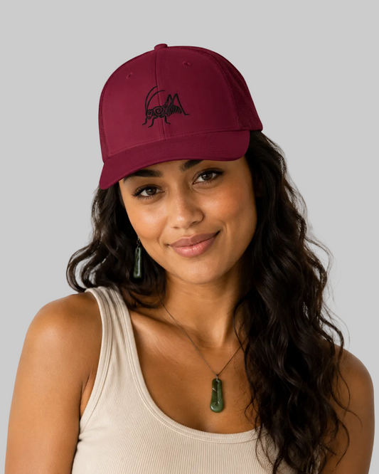 A woman with long dark wavy hair wearing a cranberry baseball cap with a black embroidered logo and a beige ribbed tank top, photographed against a clean white background.